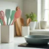 Colorful silicone kitchen tools in a modern kitchen – nonstick-safe spatulas, whisks, and spoons arranged in a pastel-themed utensil holder next to a cooking pan